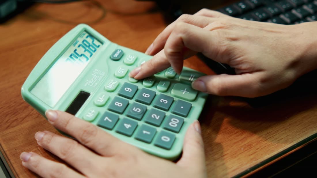 Close das mãos de uma contadora operando uma calculadora sobre a mesa de madeira