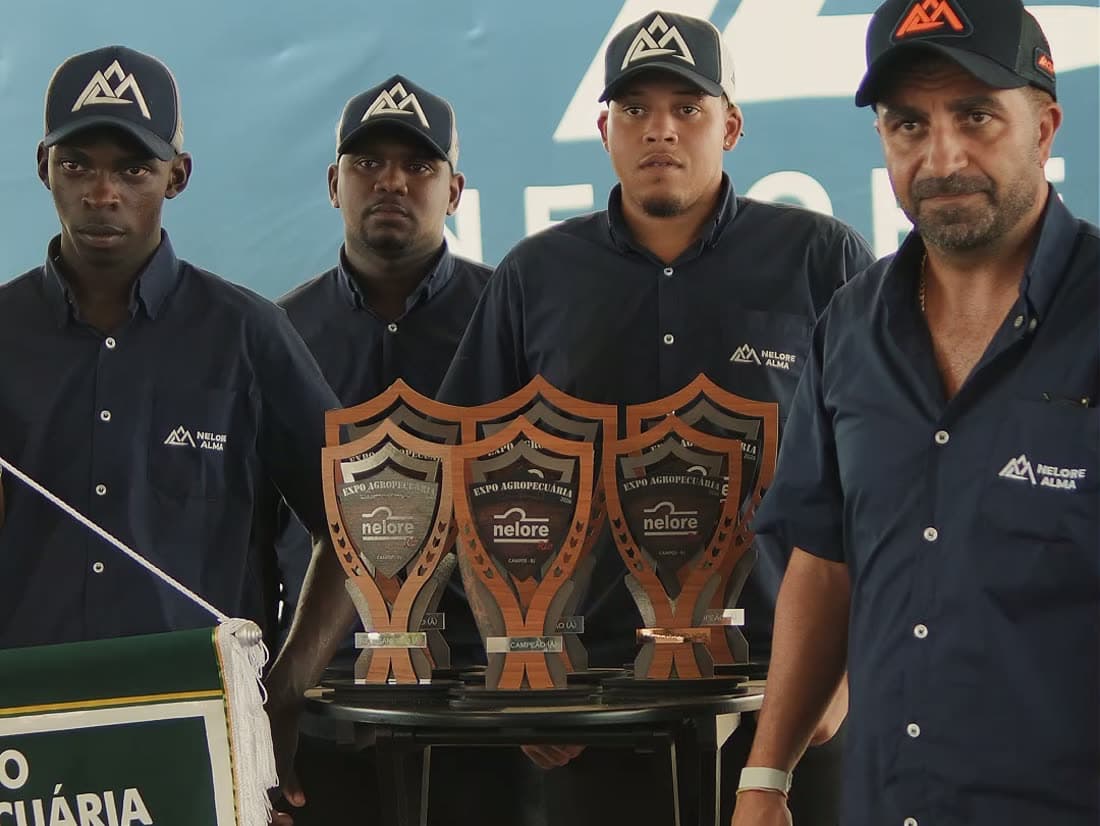 Equipe da Nelore Alma de pé atrás dos troféus e do estandarte de premiação, diante do painel da marca